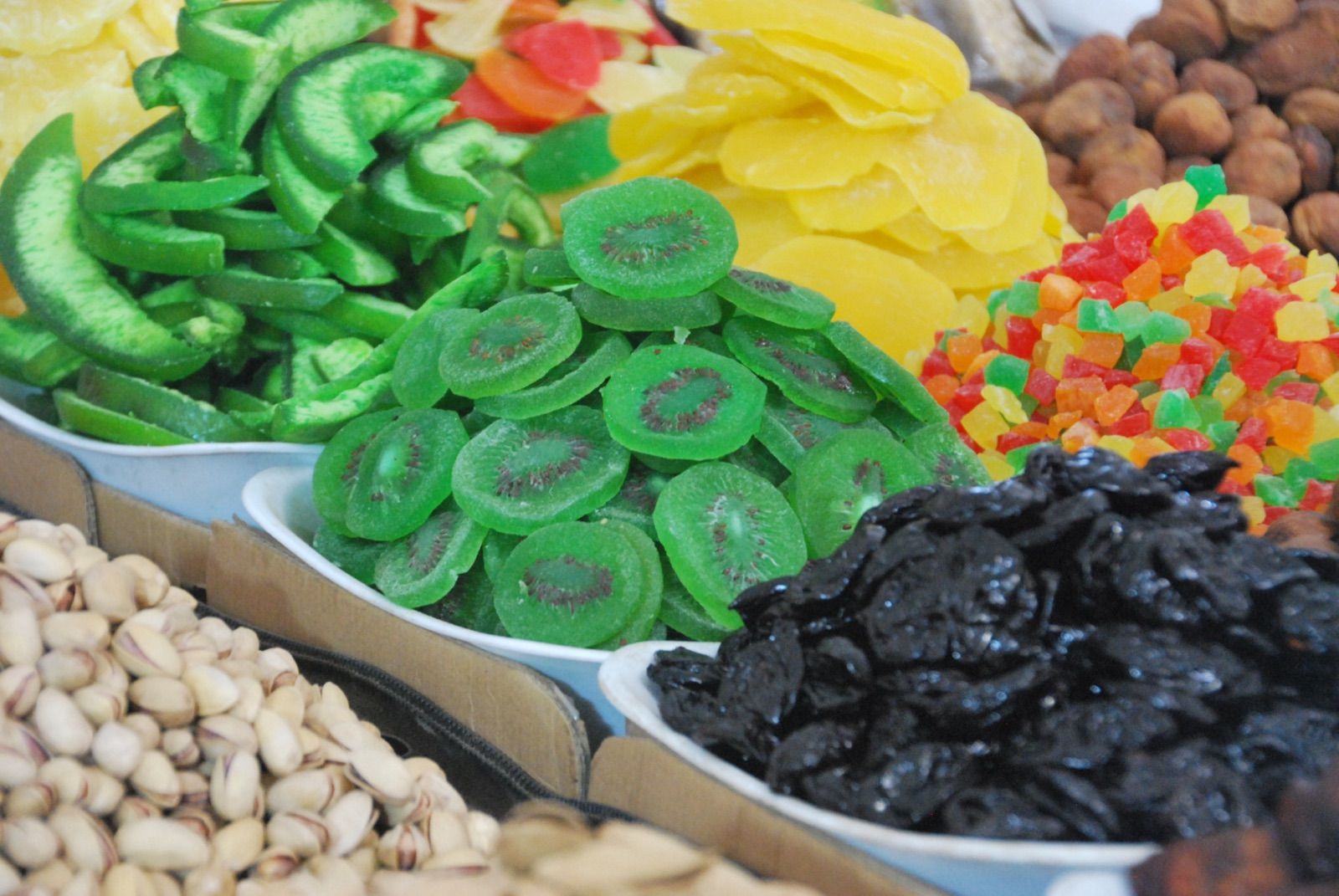 Bandejas de un puesto de bazar con kiwi y melón confitados, ciruelas pasas, pistachos y dados de fruta escarchada de colores