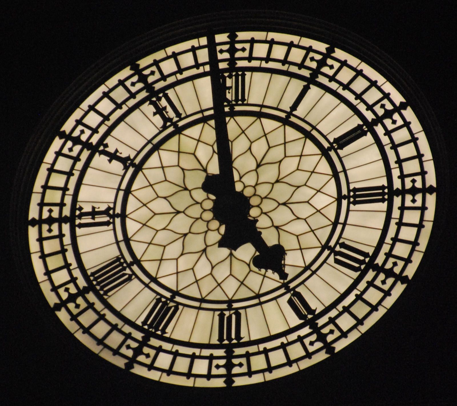 Esfera iluminada del reloj del Big Ben de noche, con números romanos y agujas negras recortadas sobre el vidrio opalino y fondo completamente oscuro