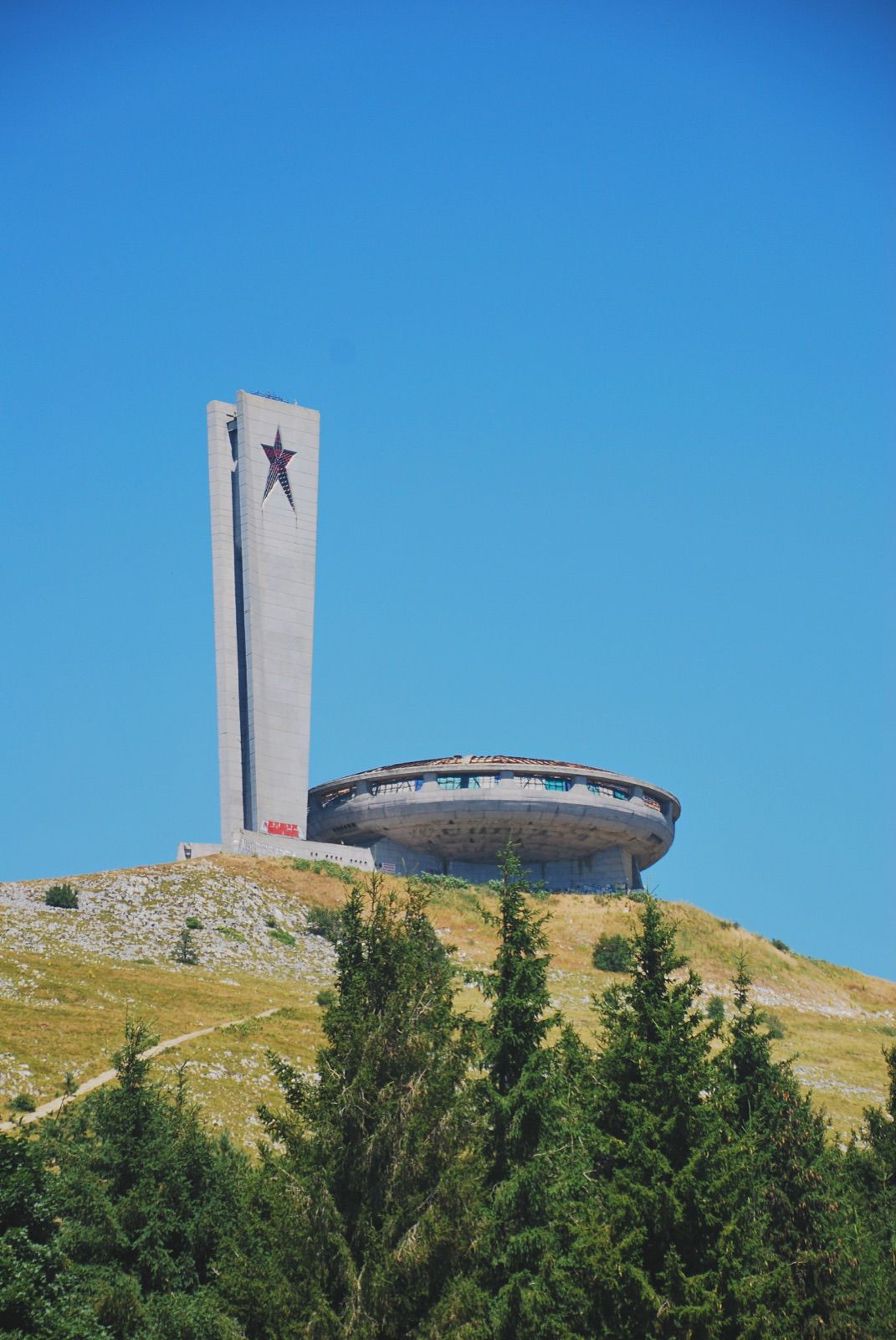 Torre y platillo del monumento de Buzludzha asomando sobre una loma con pinos
