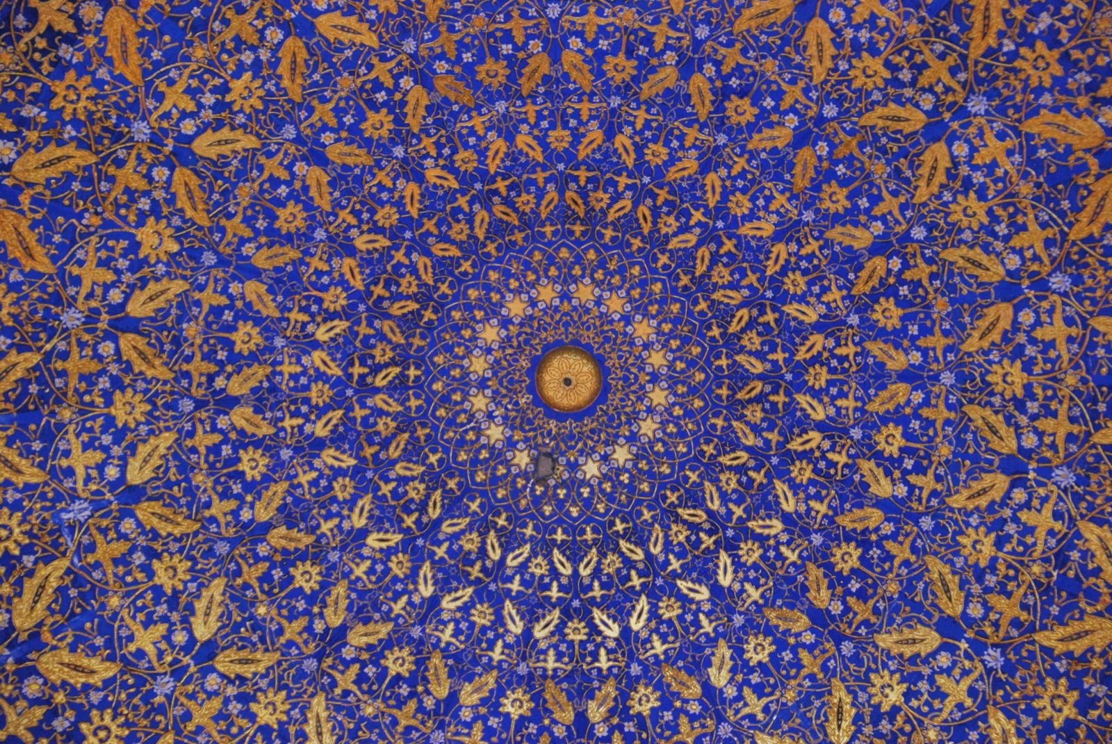 Interior de una cúpula decorada con mosaico azul cobalto y motivos vegetales dorados que giran hacia el óculo central