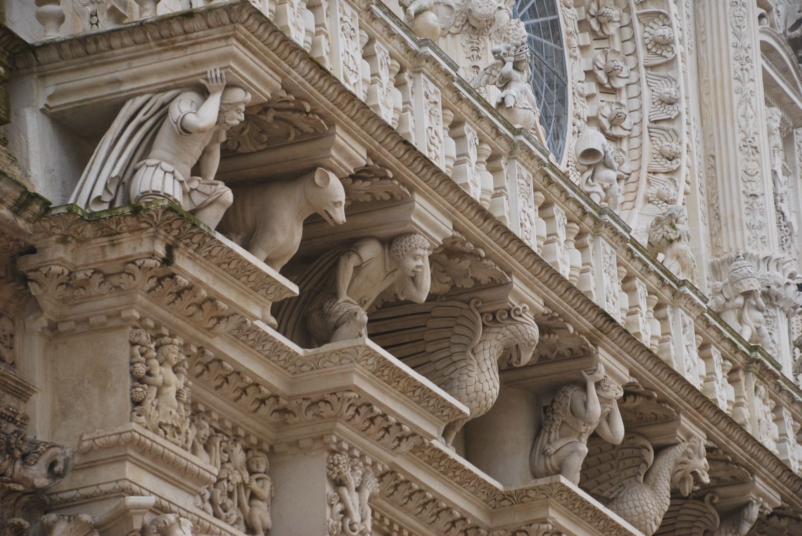 Detalle en diagonal de una cornisa barroca de Lecce con animales tallados y una figura masculina que sostiene el alero, en piedra clara