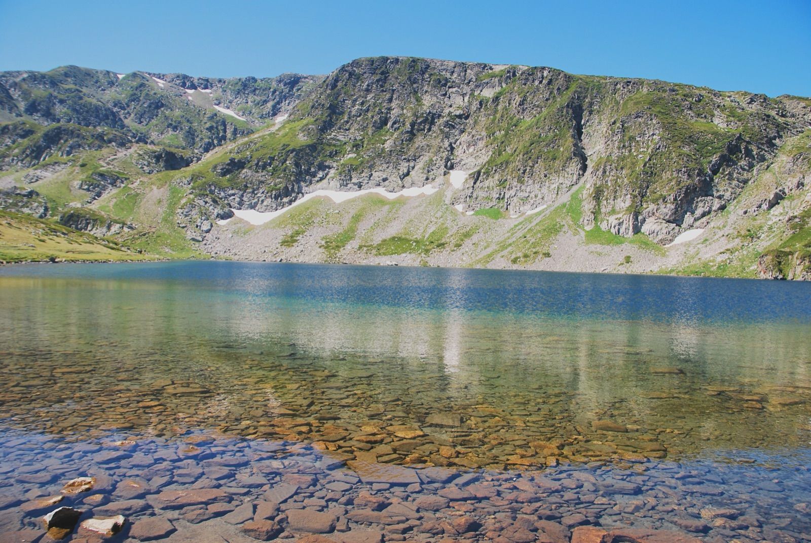 Lago glaciar de los Siete Lagos de Rila encajado en un circo de montaña con laderas de hierba