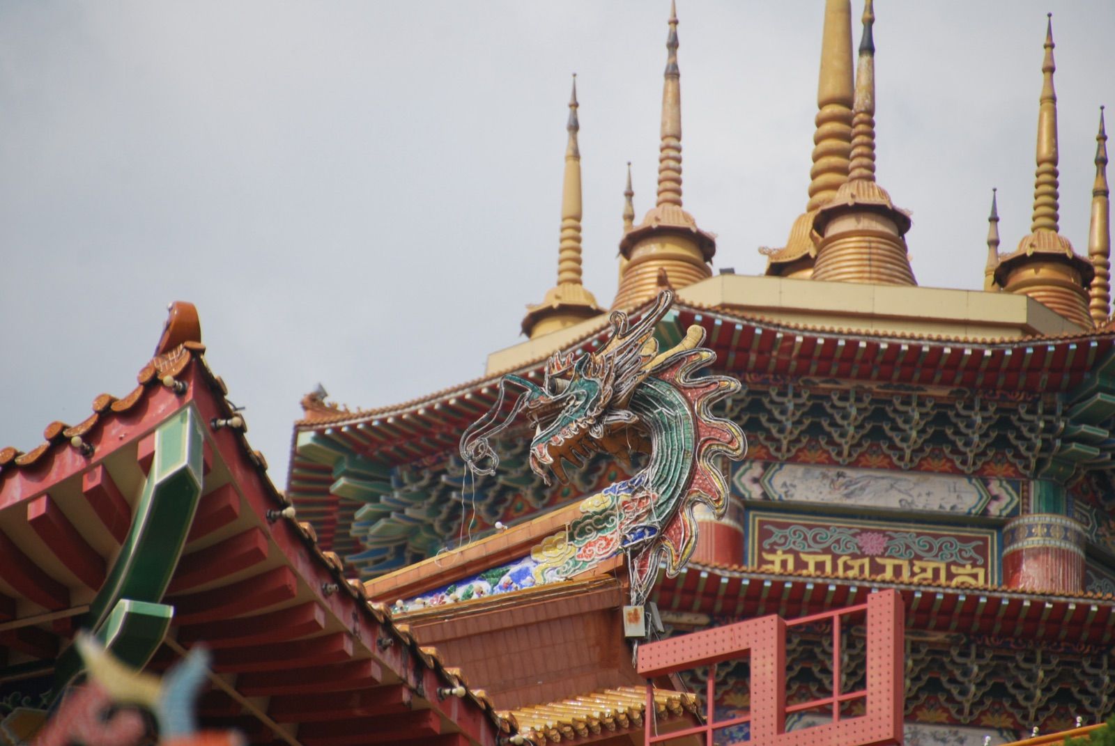 Aleros superpuestos de un templo chino con una figura de dragón policromada y, al fondo, las estupas doradas de una pagoda contra cielo blanco