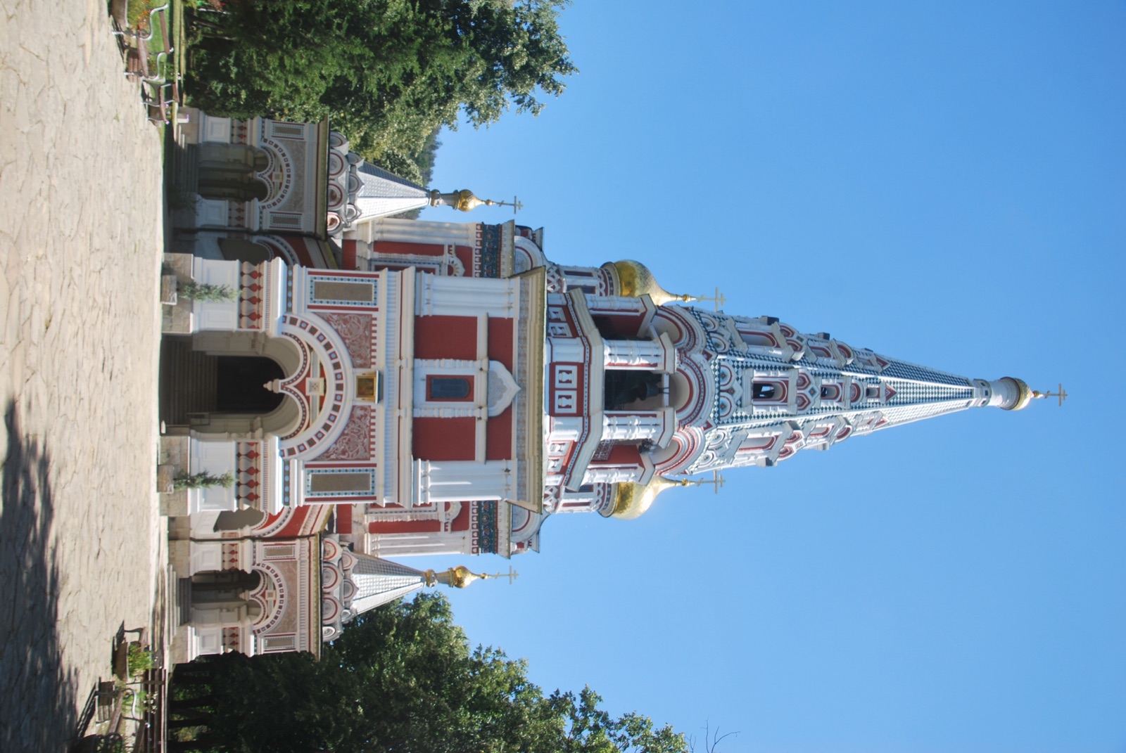 Fachada de la iglesia memorial de Shipka, de estilo ruso, con cúpulas doradas y aguja decorada frente a un cielo despejado