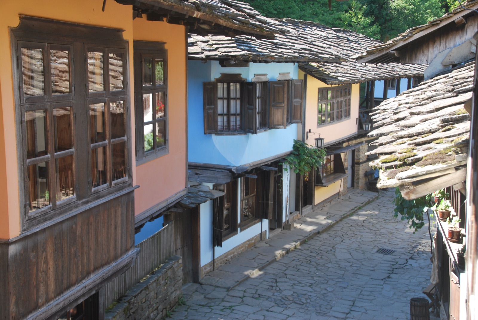 Calle empedrada del complejo etnográfico de Etar con casas de época del Renacimiento búlgaro en ocre y azul y tejados de lajas de piedra