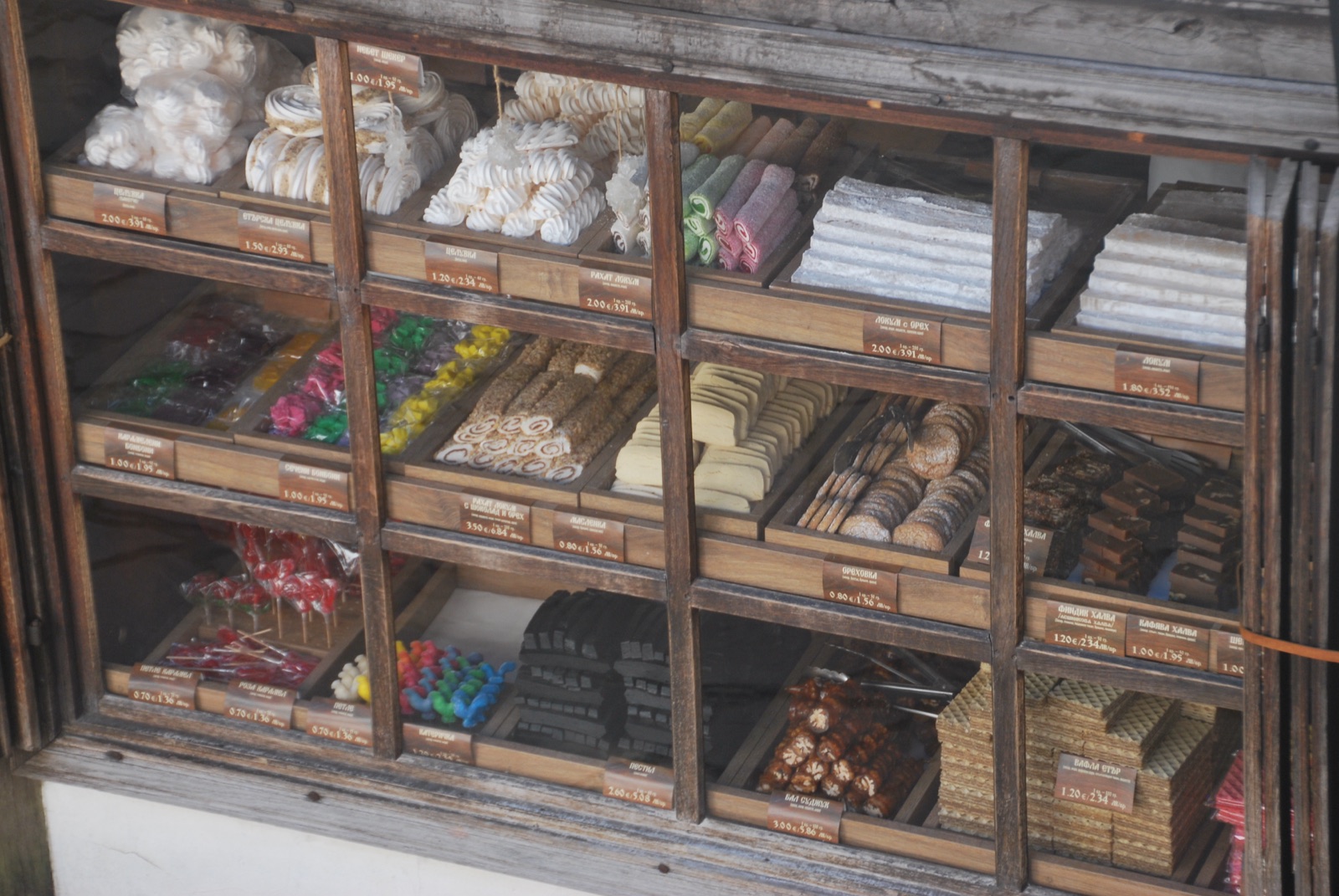 Vitrina de madera con casilleros llenos de dulces tradicionales búlgaros y etiquetas de precio a mano