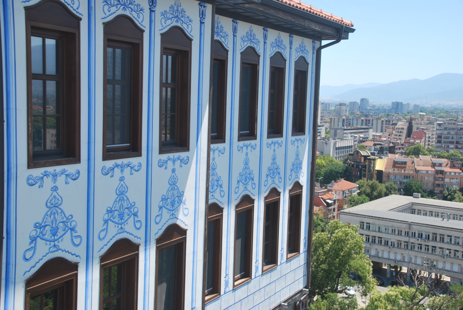 Fachada azul pintada de una casa del Renacimiento búlgaro en el casco alto de Plovdiv, con la ciudad moderna y las montañas al fondo