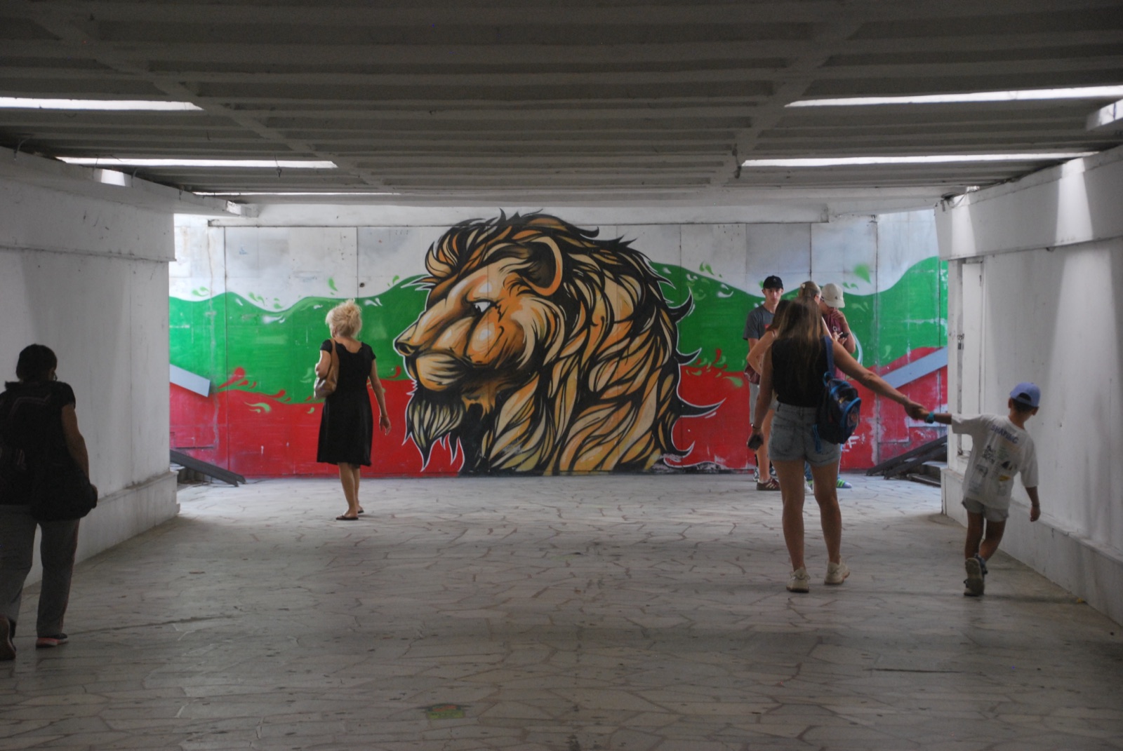 Paso subterráneo de Plovdiv con un mural de un león sobre la bandera búlgara y varios peatones cruzando