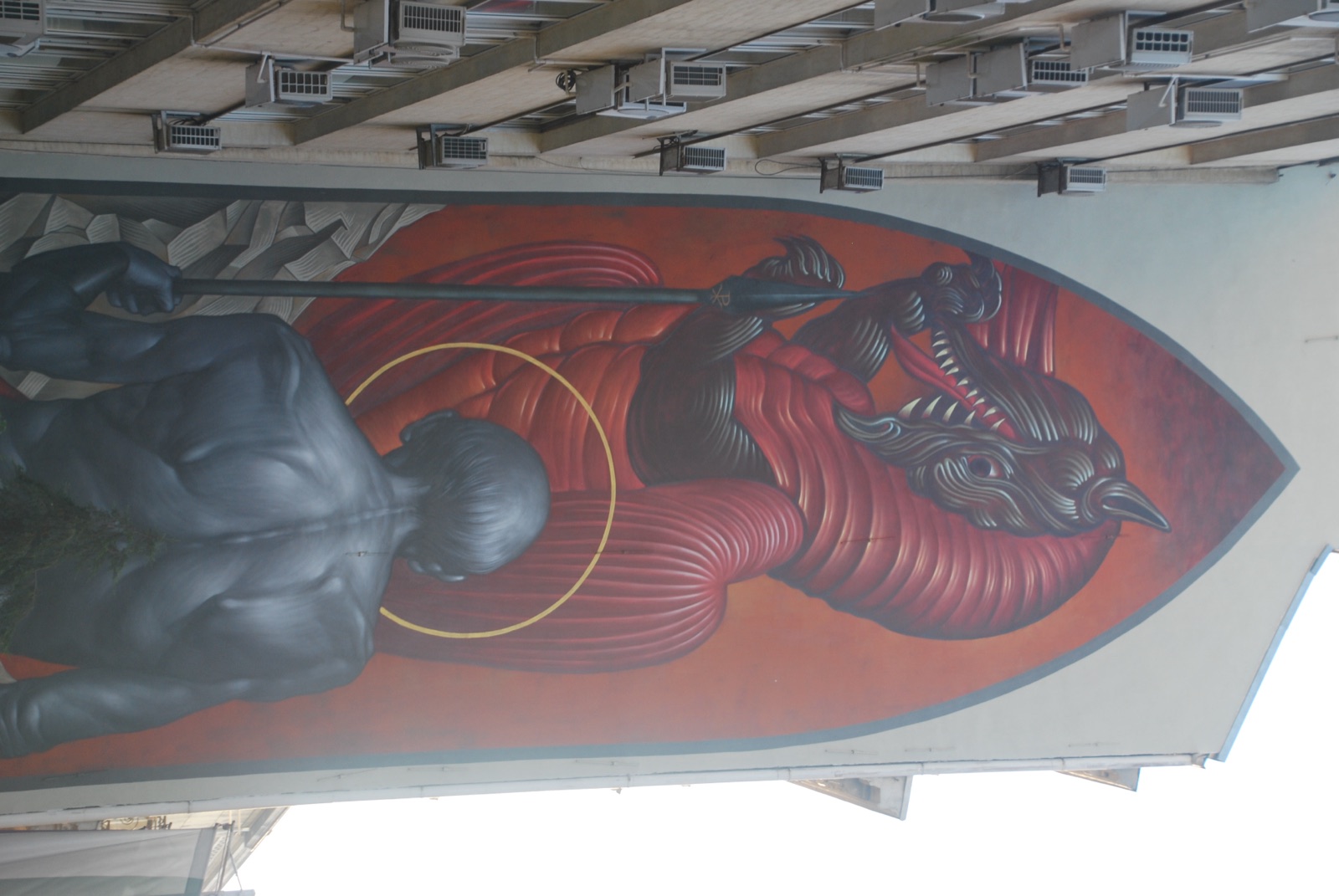 Mural de arte urbano de San Jorge y el dragón ocupando la medianera de un bloque con aires acondicionados