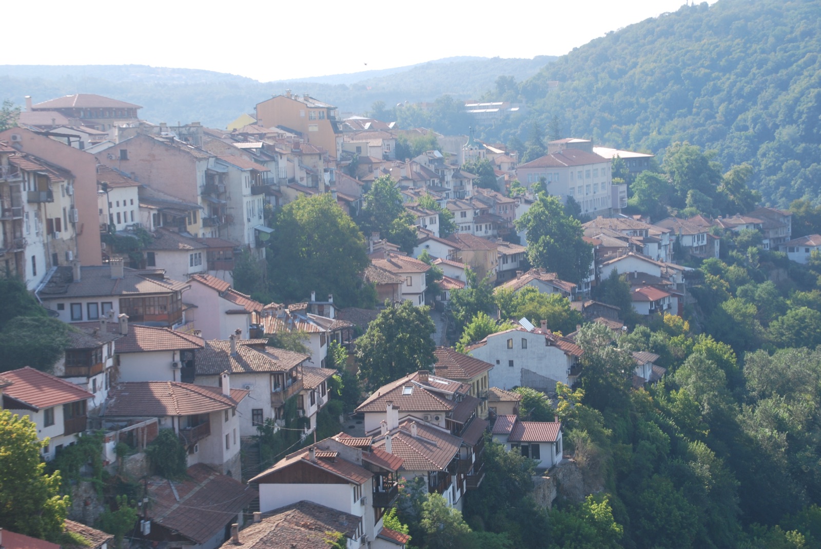 Casas de tejados rojos de Veliko Tarnovo apiladas en la ladera sobre la garganta del río Yantra, con bruma matinal