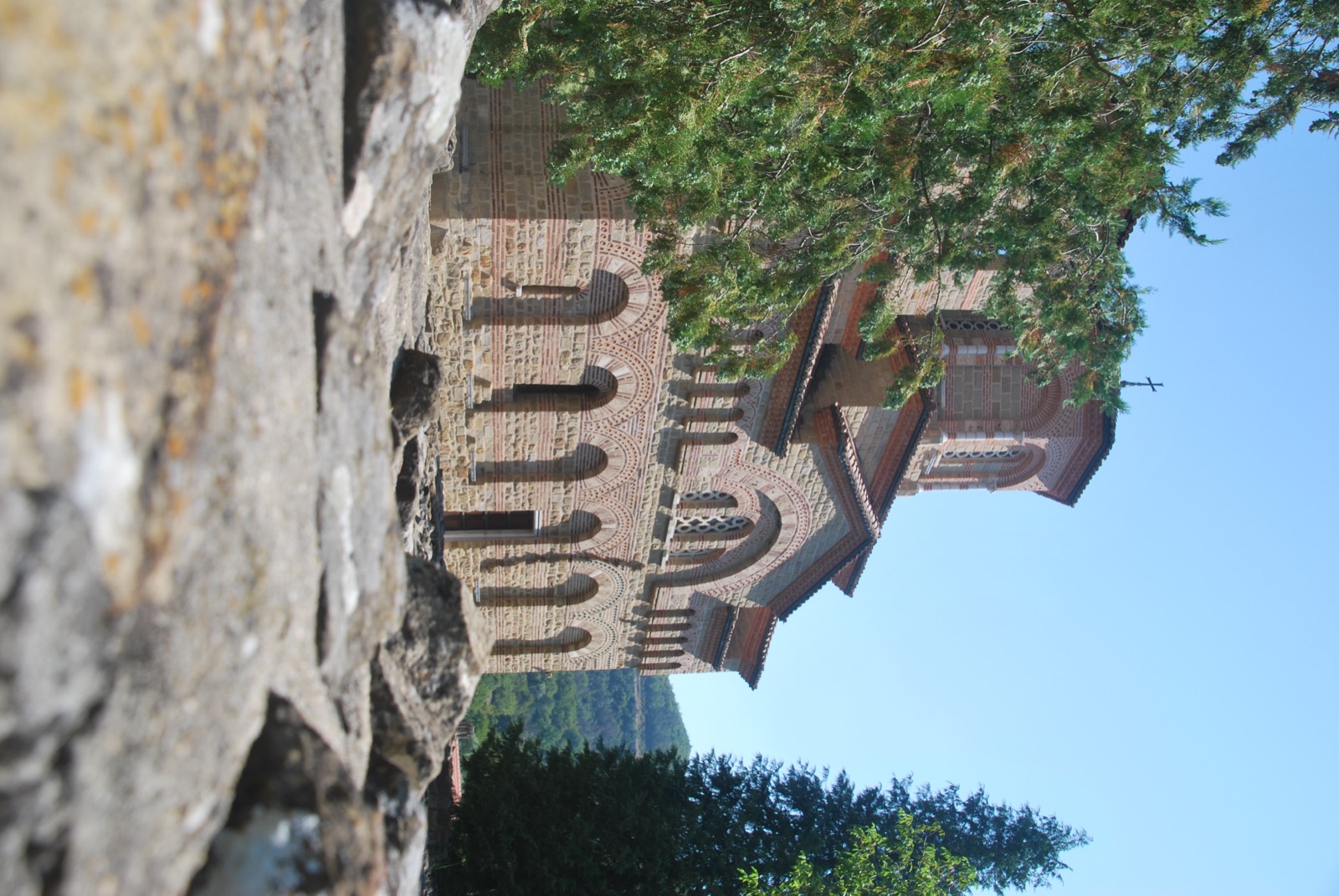 Iglesia medieval de ladrillo y piedra con arcos ciegos, fotografiada a ras de suelo entre rocas, en Veliko Tarnovo