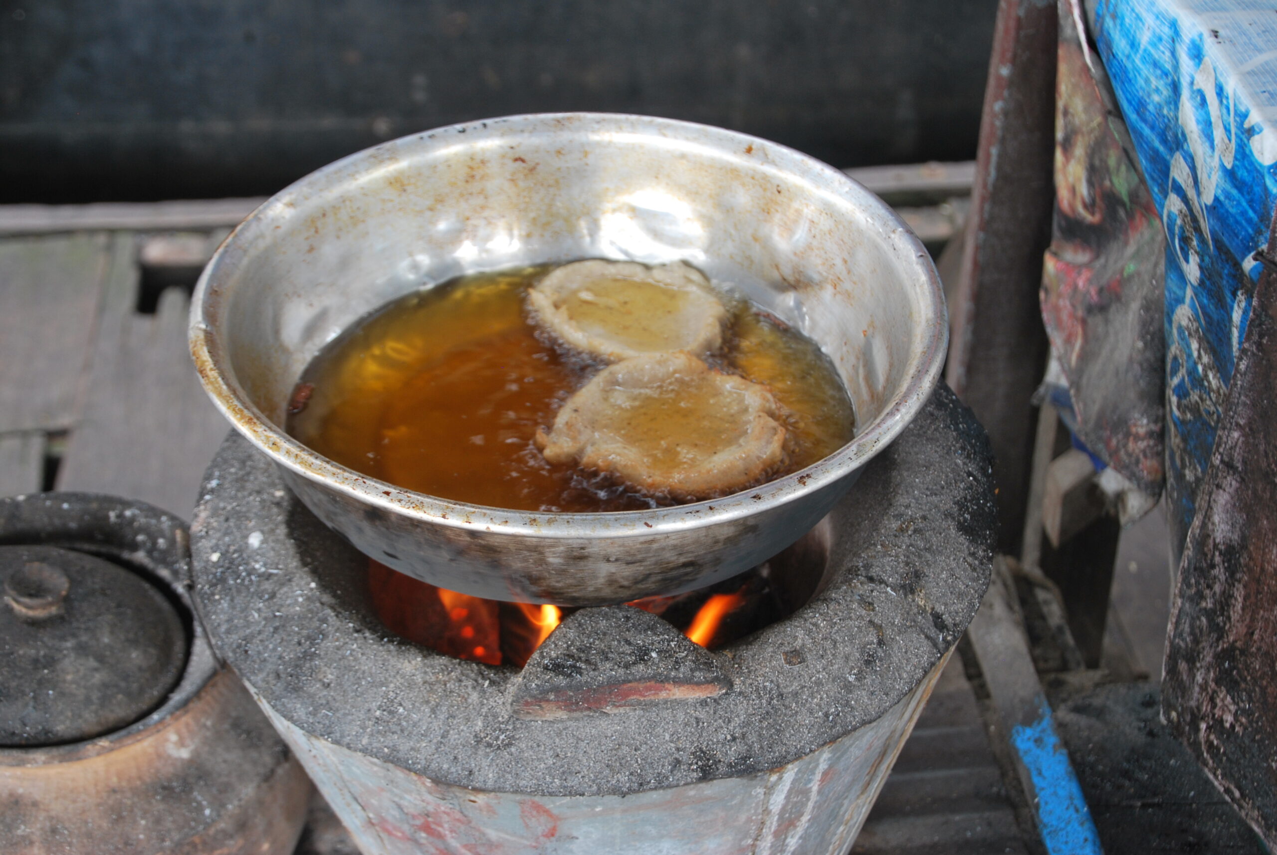 Sartén sobre horno tradicional de leña friendo dumplings en Tonlé Sap, Camboya