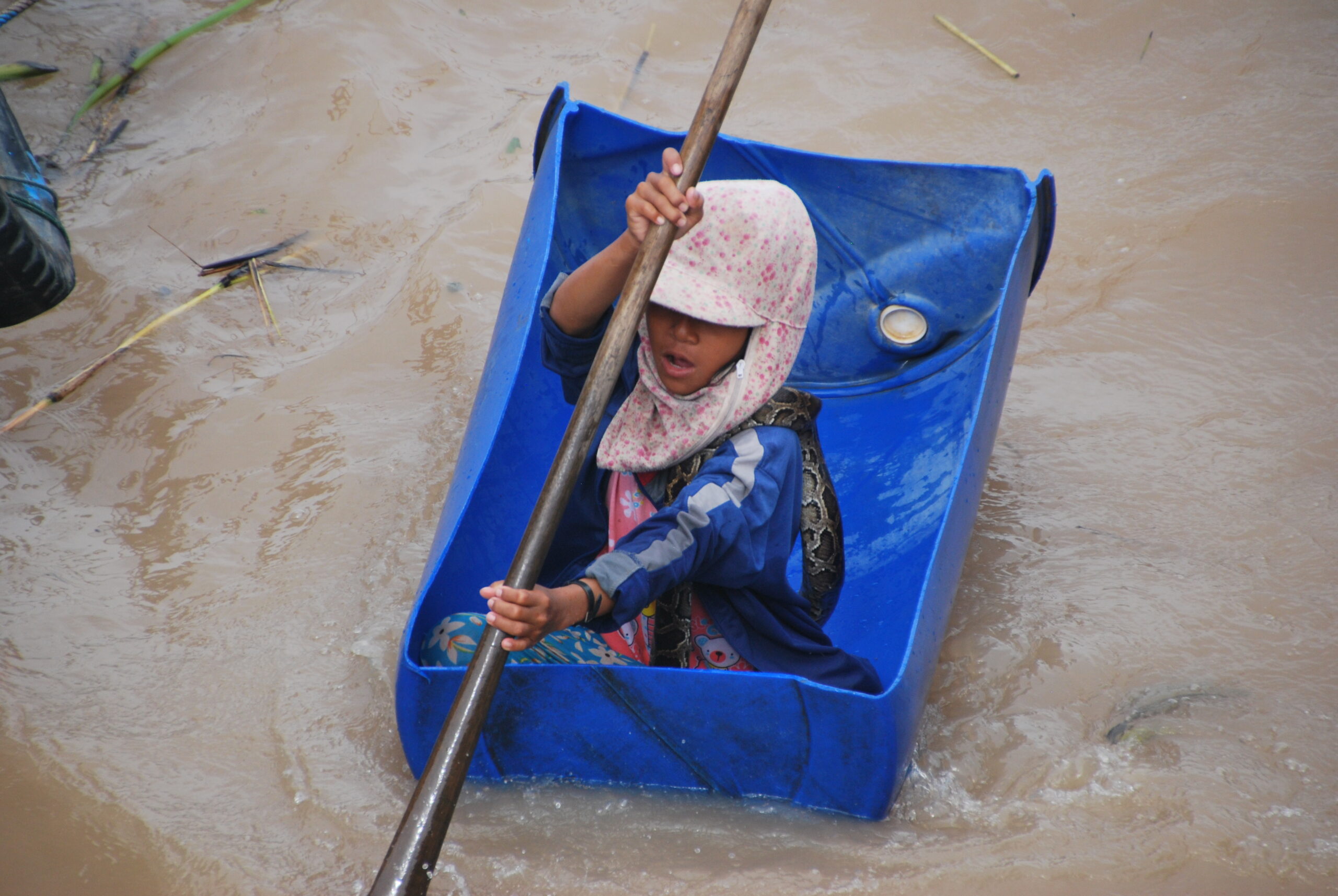 Niña camboyana remando en un barril de plástico azul con una pitón enrollada, Tonlé Sap