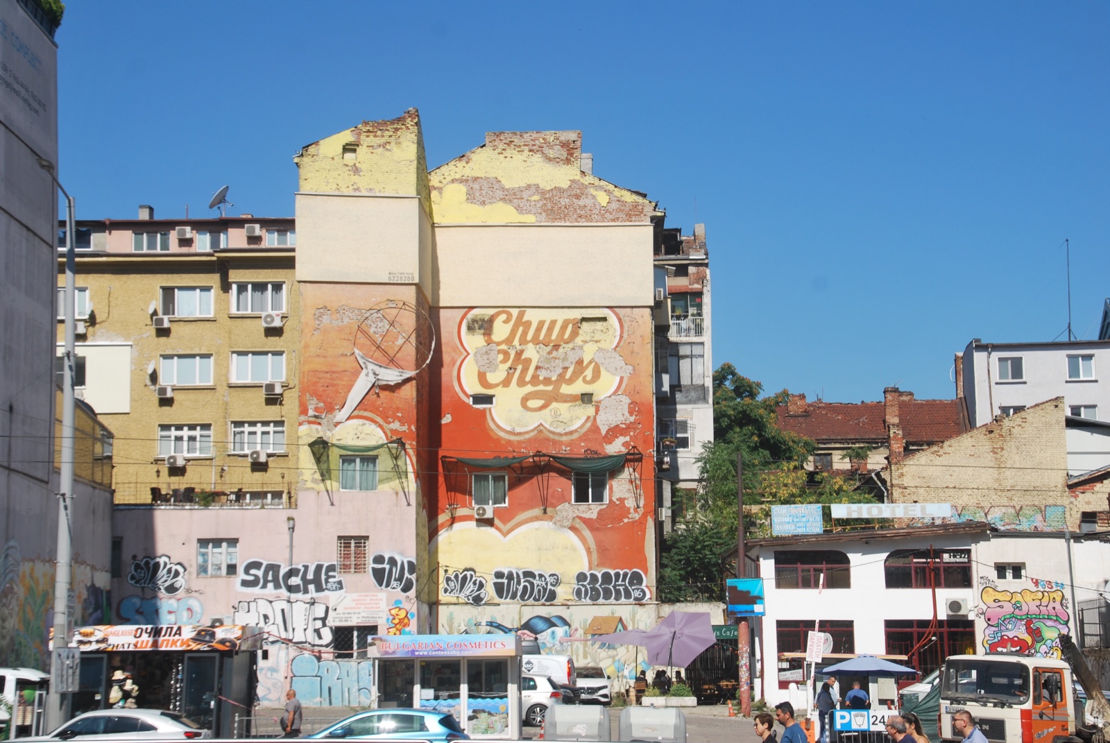 Medianera desconchada con un anuncio antiguo de Chupa Chups sobre kioscos y grafitis en el centro de Sofía