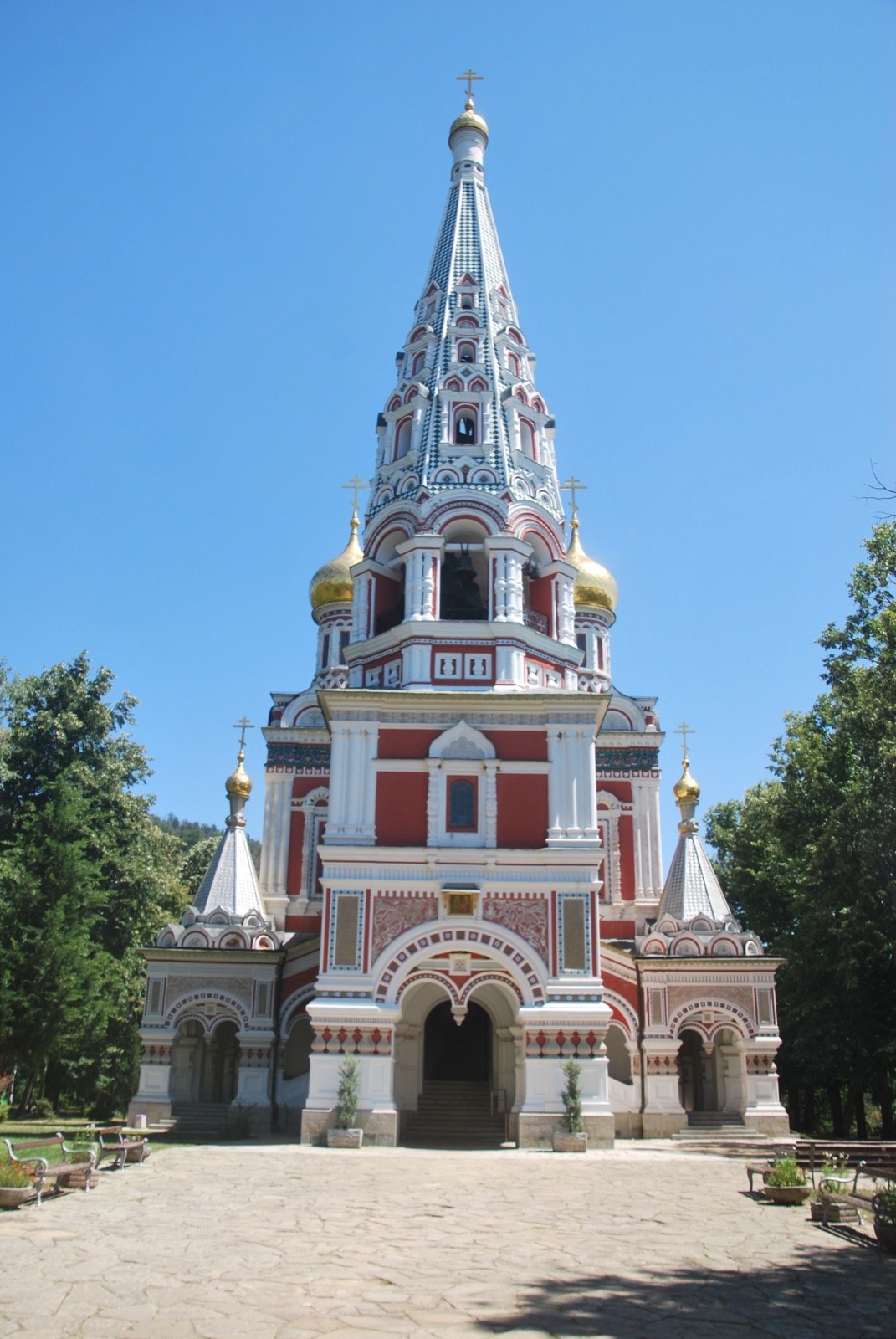 Fachada de la iglesia memorial de Shipka, de estilo ruso, con cúpulas doradas y aguja decorada frente a un cielo despejado