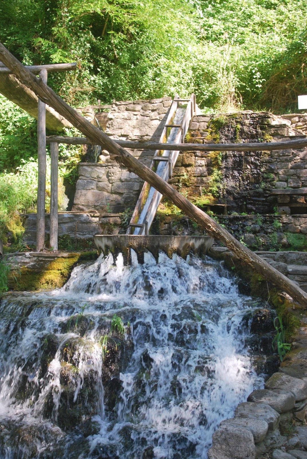 Canal de madera que vierte agua sobre una cascada entre muros de piedra en el complejo de Etar