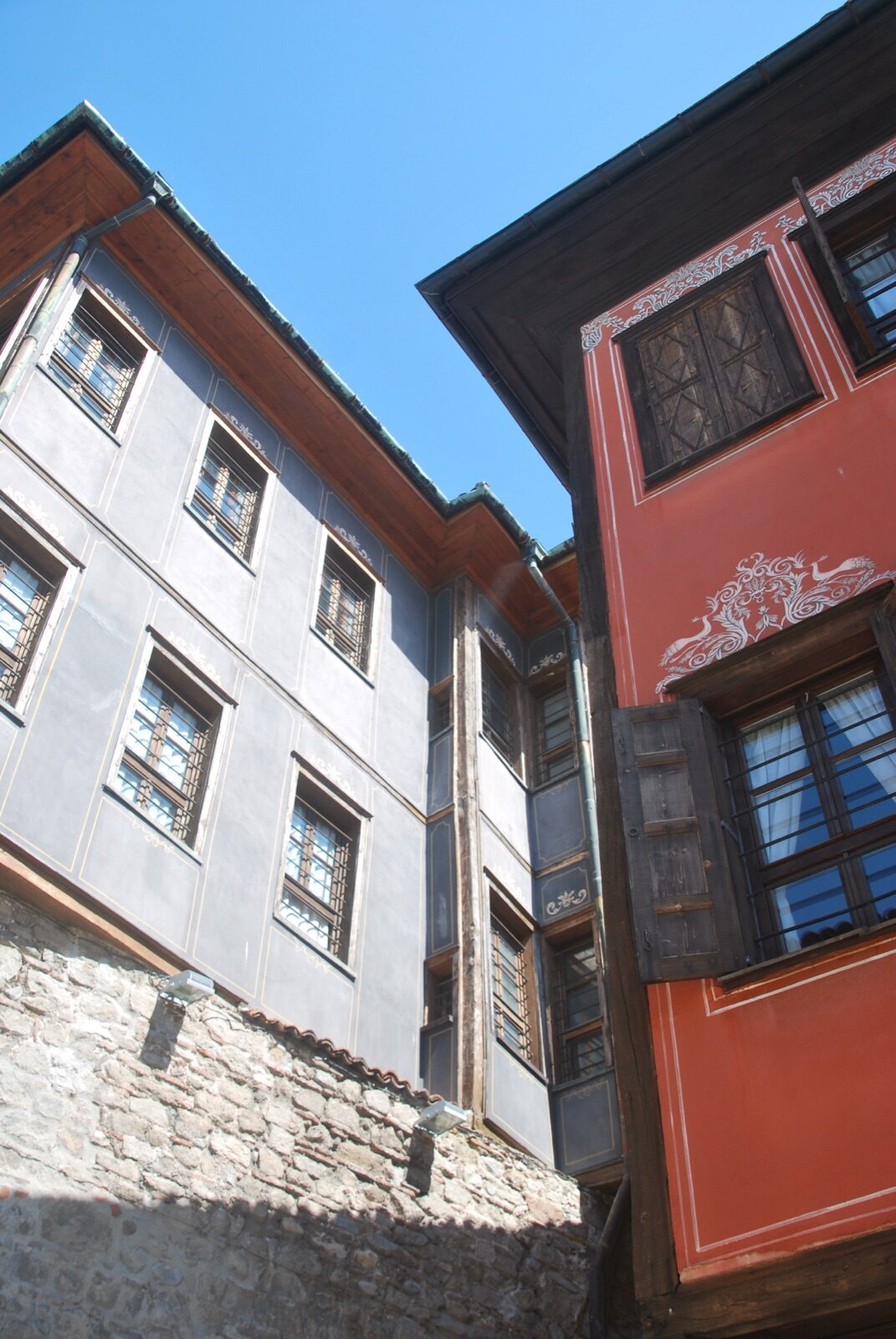 Dos casas del Renacimiento búlgaro, una gris y otra roja con decoración pintada, voladas sobre la muralla de piedra de Plovdiv