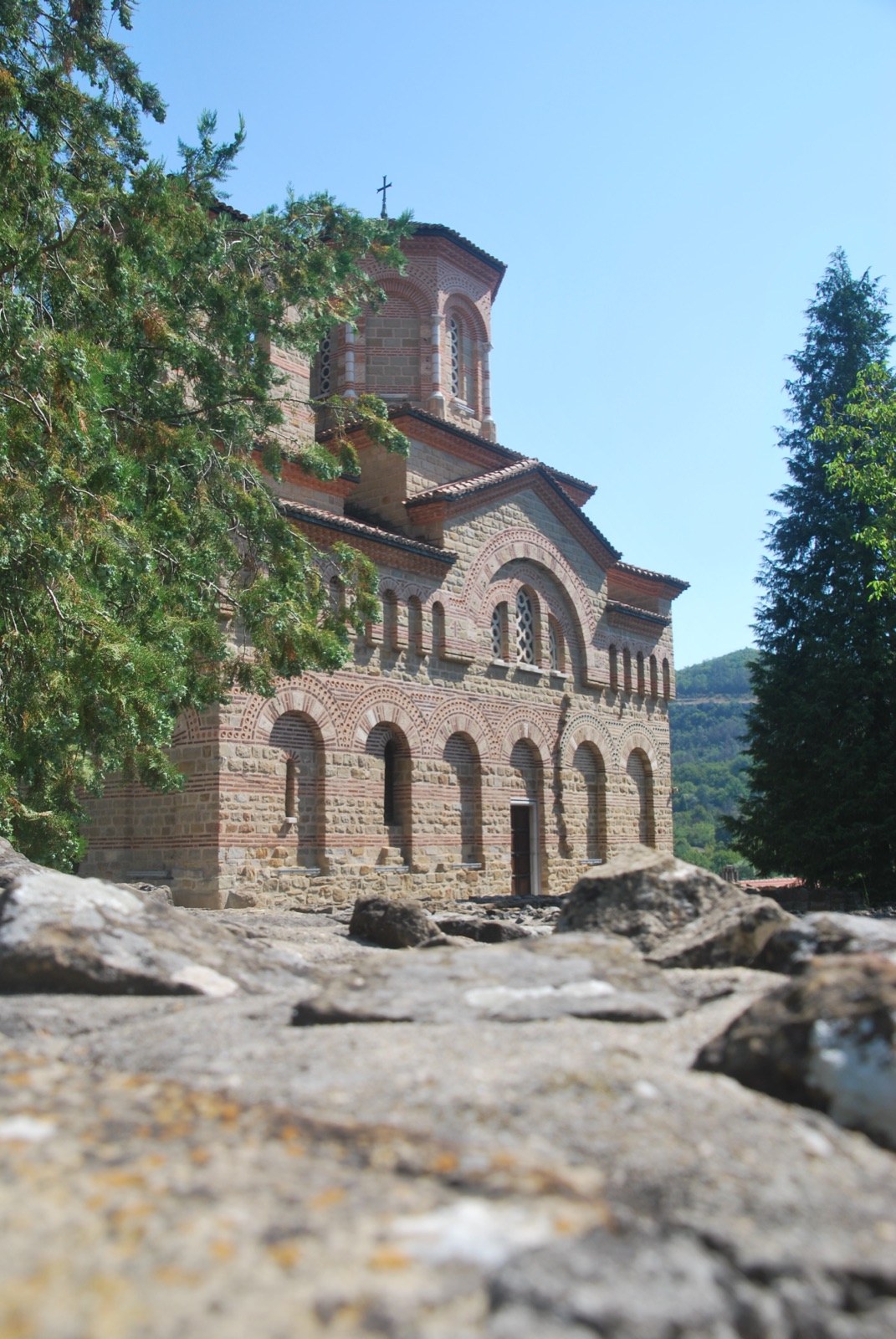 Iglesia medieval de ladrillo y piedra con arcos ciegos, fotografiada a ras de suelo entre rocas, en Veliko Tarnovo
