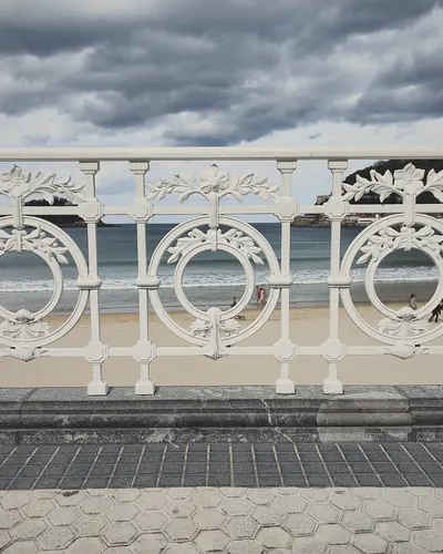 Barandilla blanca ornamentada frente a la playa, bajo un cielo nublado