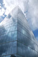 Rascacielos de cristal visto desde abajo, con nubes reflejadas en la fachada