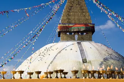 Estupa de cúpula blanca y torre dorada con los ojos de Buda, con cuerdas de banderas de oración y una hilera de lamparillas en la base